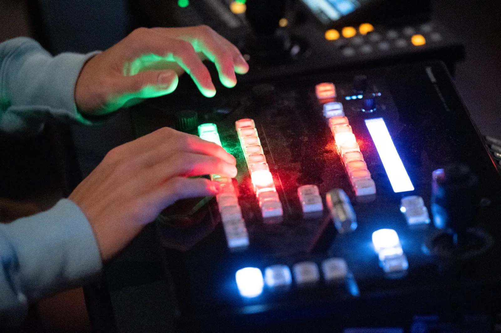 Two hands working an illuminated tech desk during a service, its buttons lit green, red and white